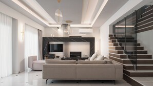 A modern living room with a sofa, TV, and staircase. - Villa Kalliston - 4000m2 of Elevated Living (Rethymno)