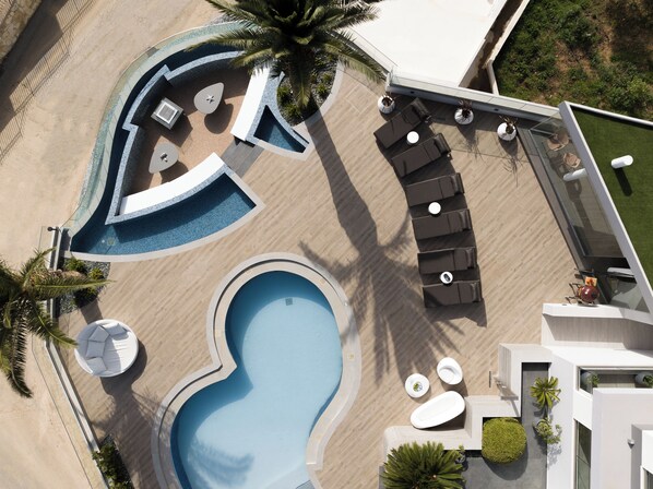 An aerial view of a resort with a swimming pool, sun loungers, and a palm tree.