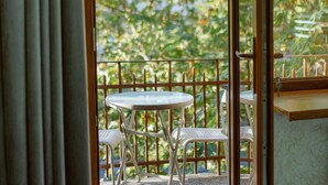 A balcony with a table and chairs, a view of trees, and a wooden railing. - Opera Avenue Hotel Yerevan (Yerevan)