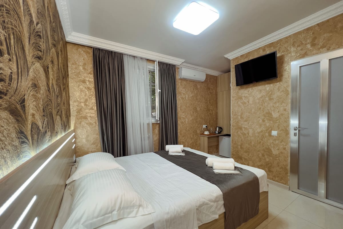 A hotel room with a bed, a TV, a desk with a kettle, and a wardrobe.