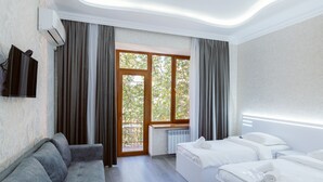 A hotel room with a grey sofa, two single beds, a TV mounted on the wall, and a large window with curtains. - Opera Avenue Hotel Yerevan (Yerevan)