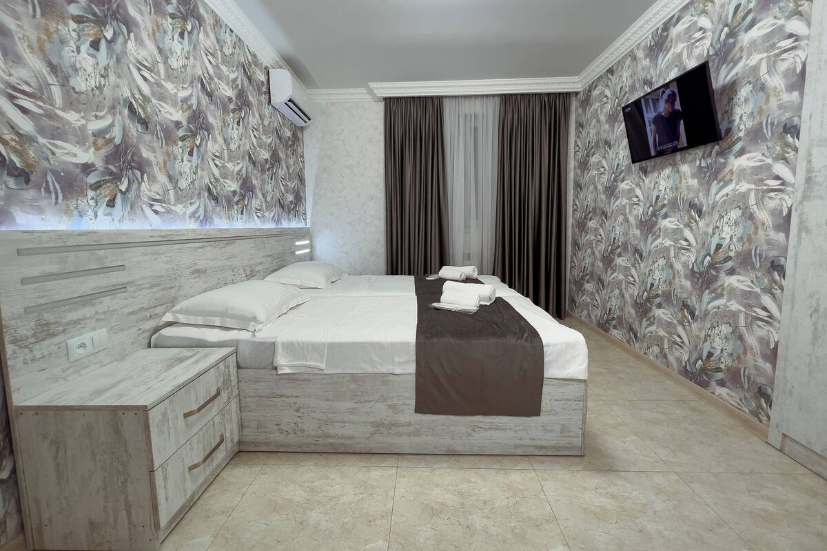 A bedroom with a bed, a TV, a wardrobe, and a window with curtains.
