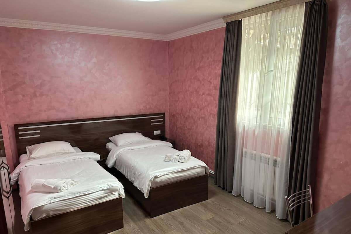 A hotel room with two beds, a wooden floor, and a large window with sheer curtains.