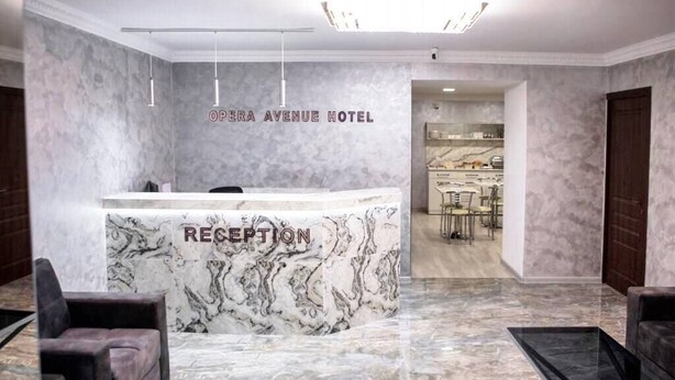 A marble reception desk with "RECEPTION" and "OPERA AVENUE HOTEL" signage, a modern interior with a kitchen visible in the background. - Opera Avenue Hotel Yerevan (Yerevan)