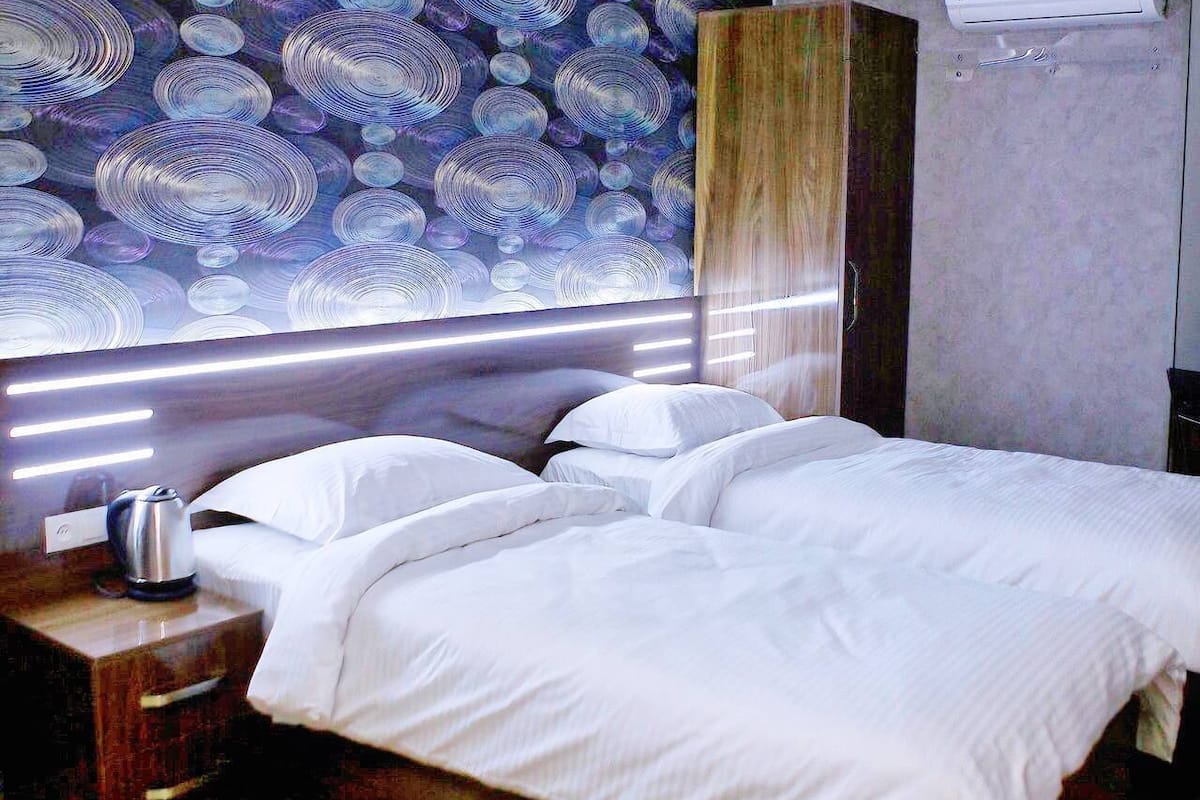 A hotel room with a bed, a nightstand, a kettle, and a wall with circular patterns.