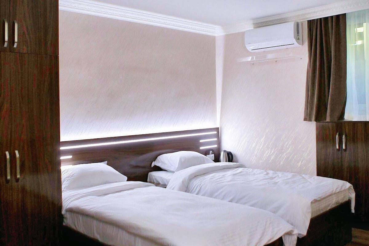 A hotel room with two single beds, a wooden wardrobe, and a window with curtains.