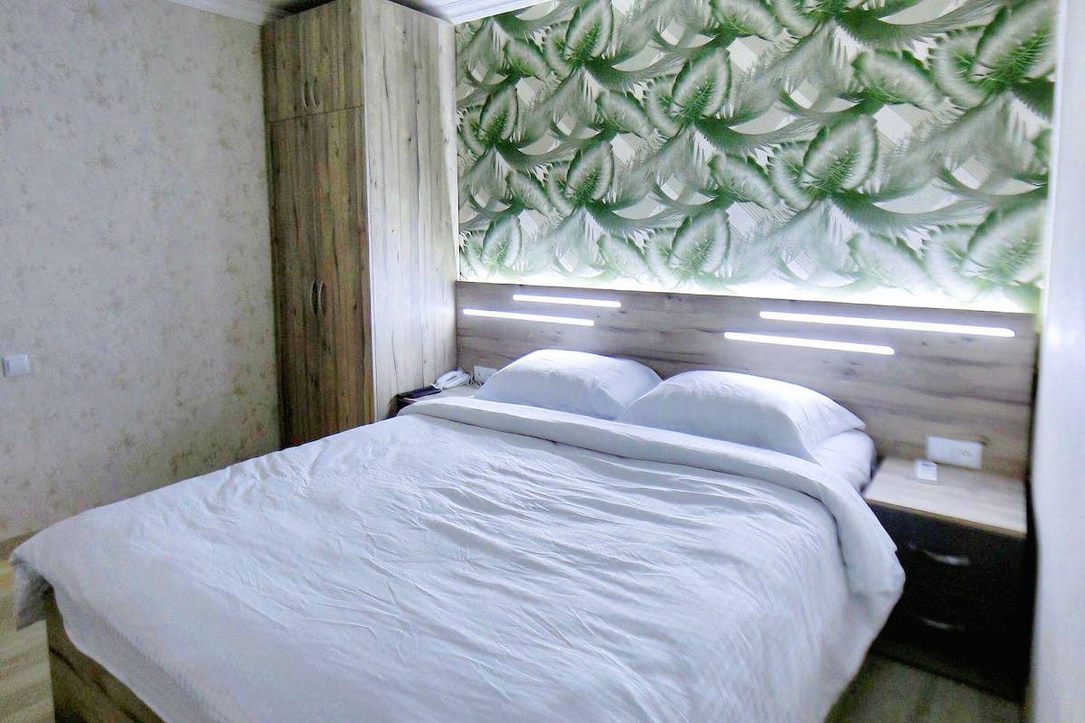 A bed with white bedding, a wooden headboard, and a nightstand with a lamp.