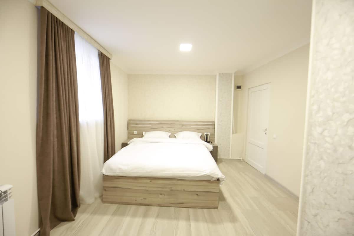 A bedroom with a wooden bed, white bedding, a nightstand, a bedside table, and a door.