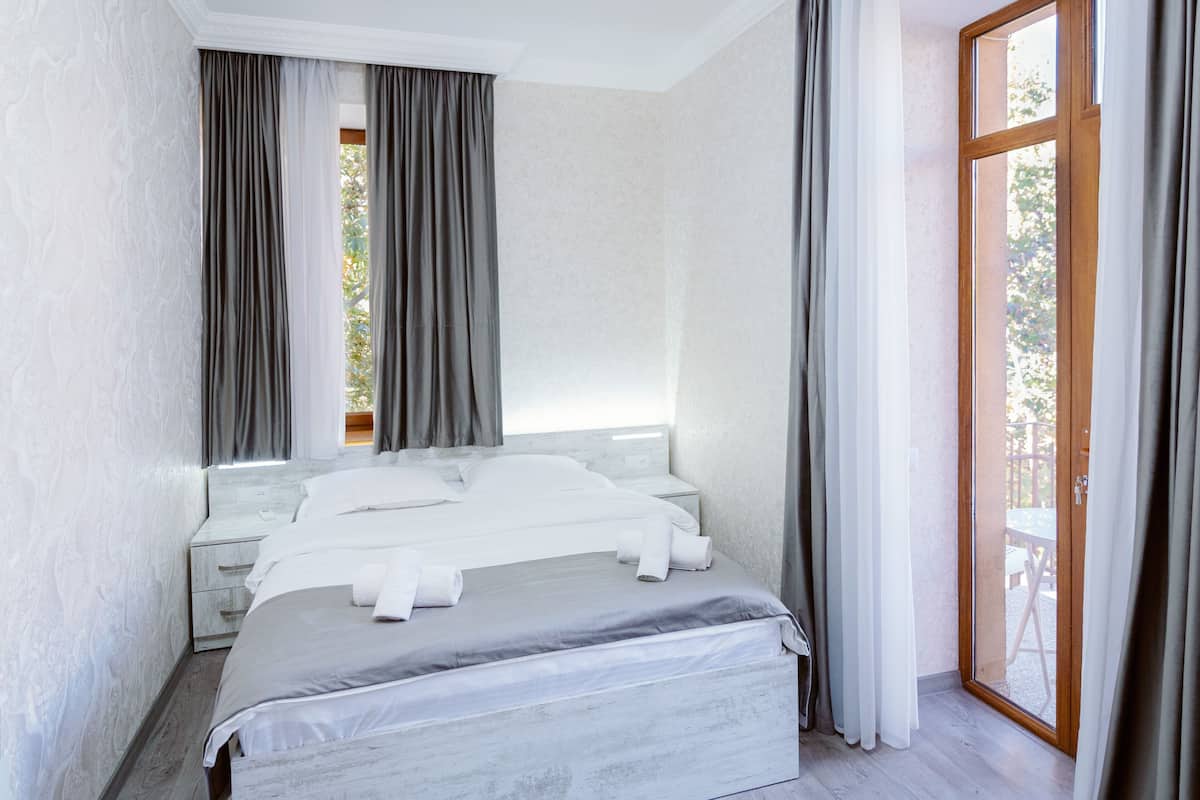A modern bedroom with a large bed, a nightstand, and a view of the outdoors through a glass door.