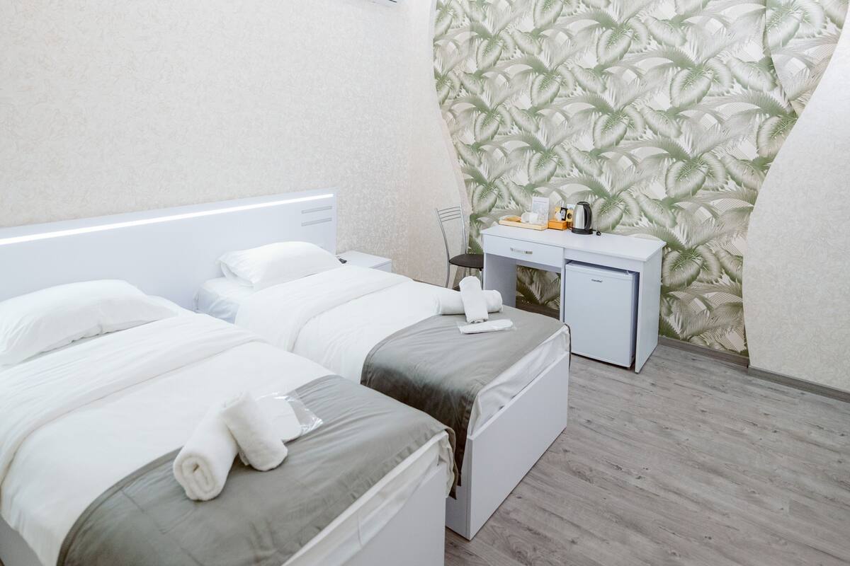 A hotel room with two beds, a desk, a small fridge, and a patterned wall.
