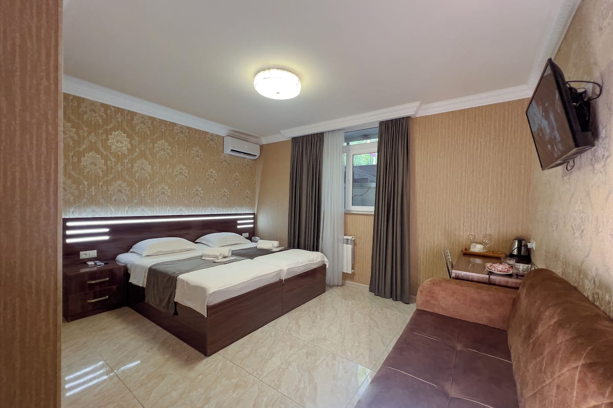 A hotel room with a bed, bedside tables, a TV mounted on the wall, and a small seating area with a couch.