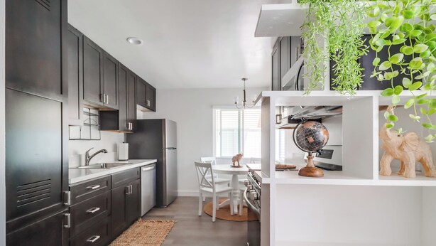 A modern kitchen with dark cabinets, white countertops, a dining area with a round table and chairs, and a globe on a shelf. - Majestic Coastal Retreat in Coronado (Coronado)