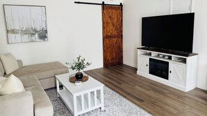 A living room with a sofa, coffee table, TV, fireplace, and a wooden door. - Majestic Coastal Retreat in Coronado (Coronado)