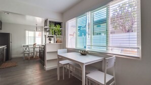 A modern kitchen with white cabinetry, a dining table with chairs, and a window with blinds. - Majestic Coastal Retreat in Coronado (Coronado)