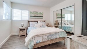 A bedroom with a large bed, a nightstand with a lamp, a mirror, and artwork on the wall. - Majestic Coastal Retreat in Coronado (Coronado)
