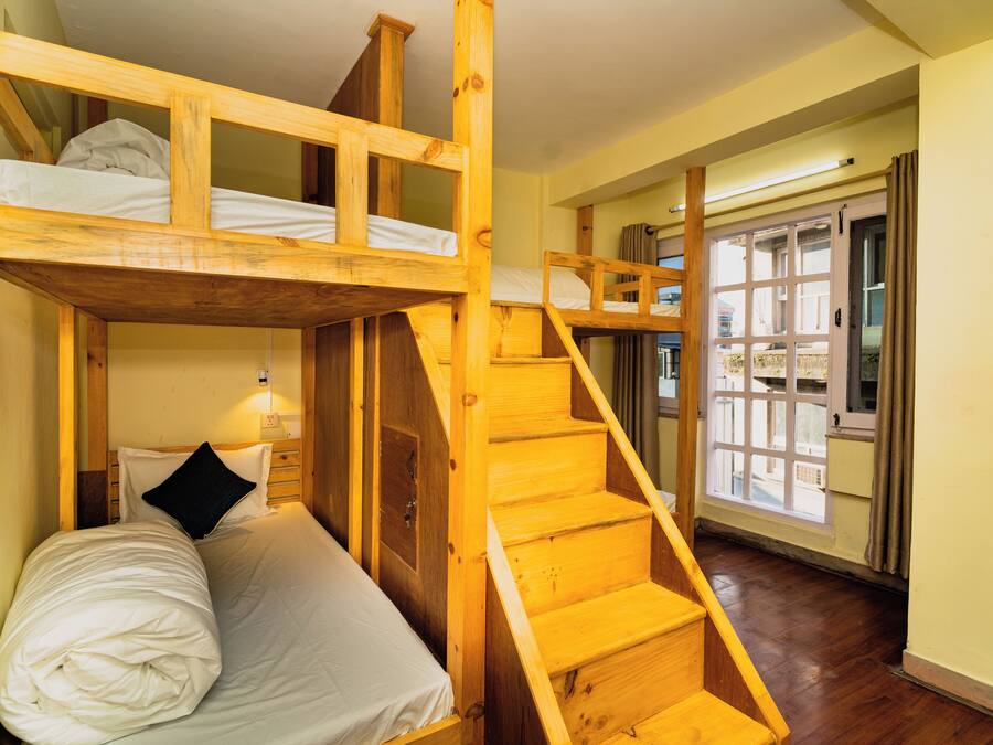 Habitación con literas, escalera de madera y ventana con cortinas.