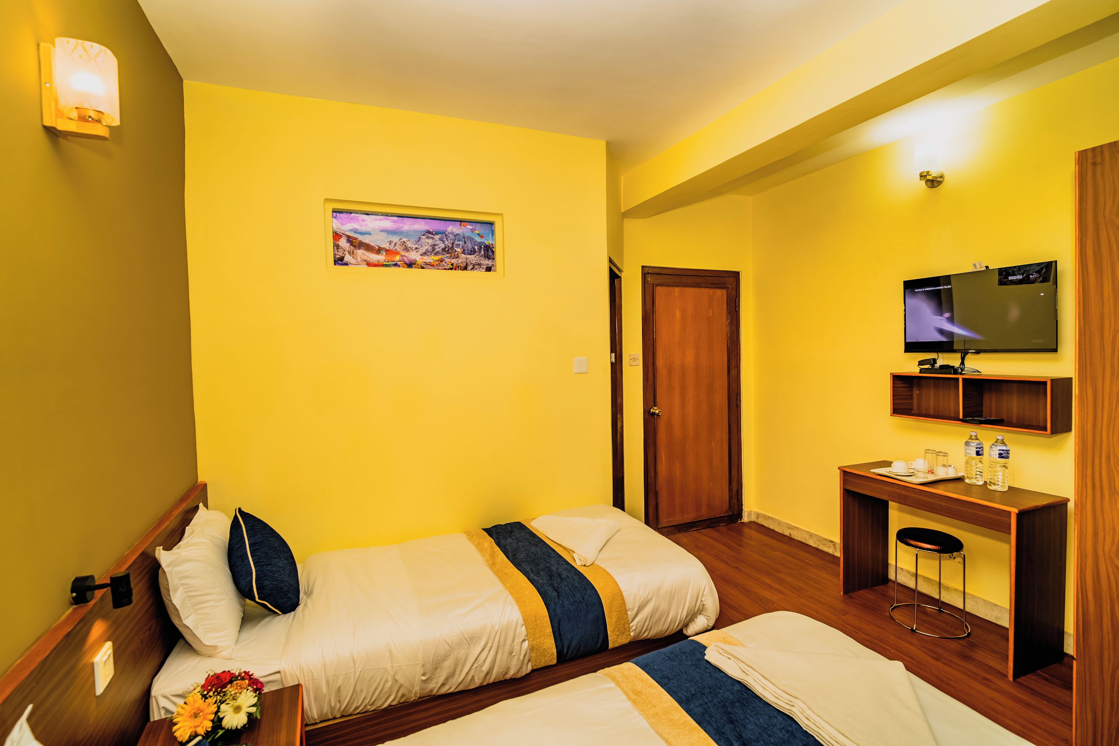A hotel room with two beds, a desk, a TV, and a painting on the wall.