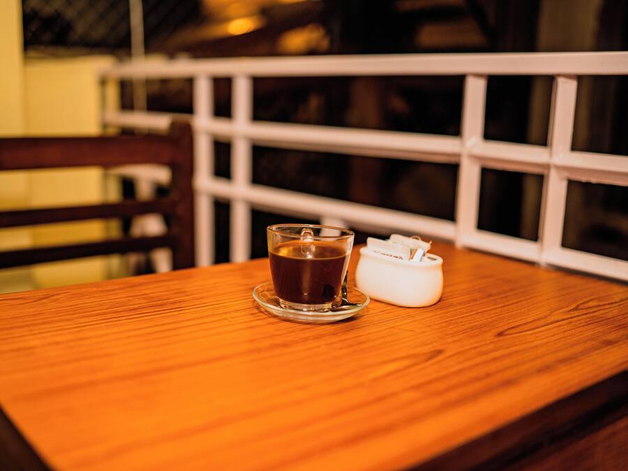 Una mesa de madera con una taza de té y un pequeño recipiente blanco, probablemente para azúcar o leche, en un restaurante.