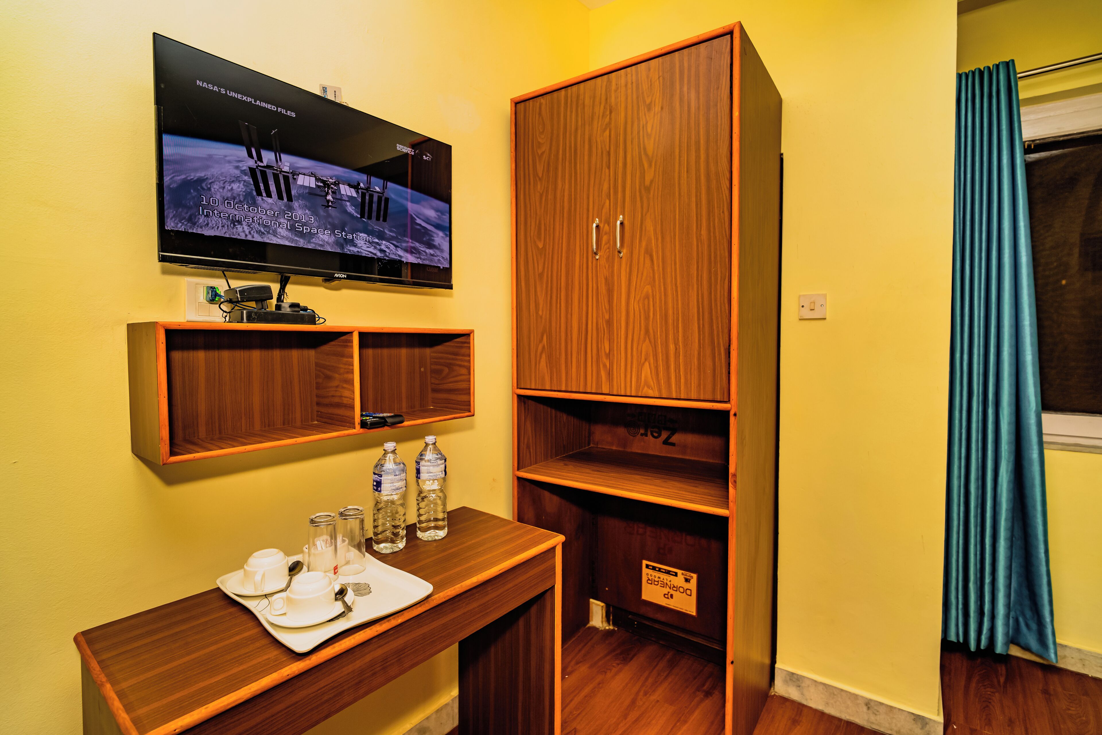 Quarto de hotel com secretária de madeira, televisão na parede e guarda-roupa.