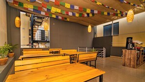 A room with wooden benches, a coffee machine, and prayer flags on the ceiling. - Hotel Aashraya Home Pvt. Ltd.  (Kathmandu)