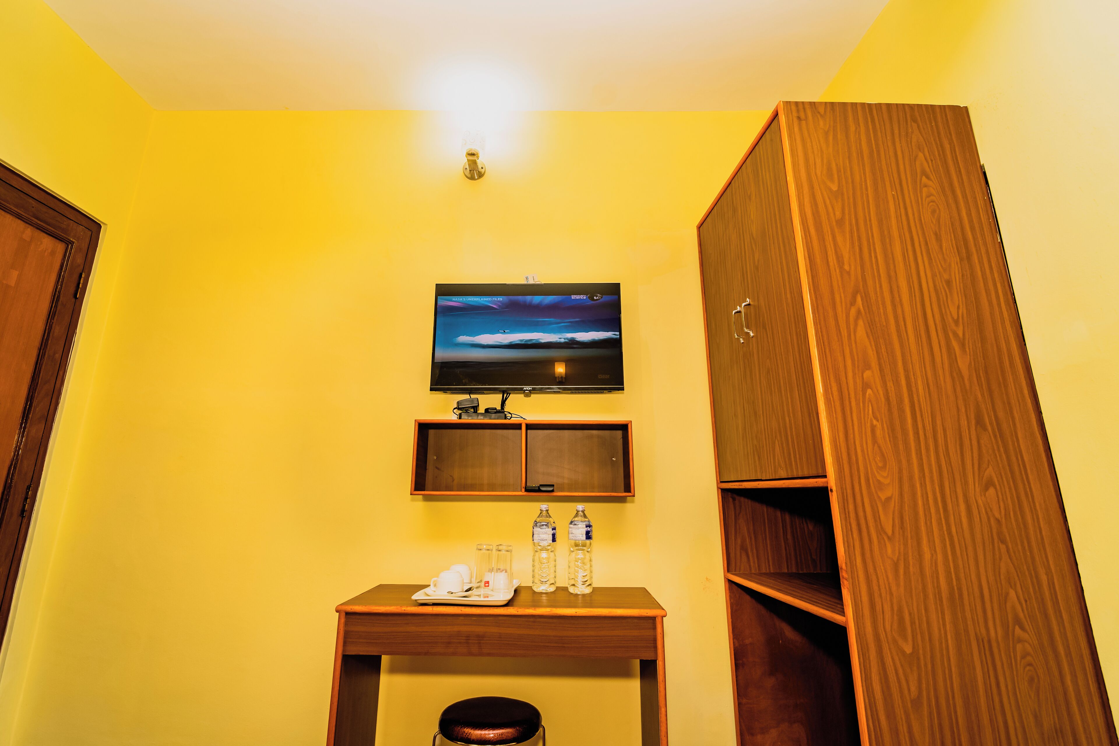 Une chambre d’hôtel avec un bureau en bois, un téléviseur fixé au mur et une armoire.