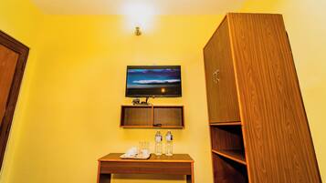 Una habitación de hotel con un escritorio de madera, un televisor montado en la pared y un armario.