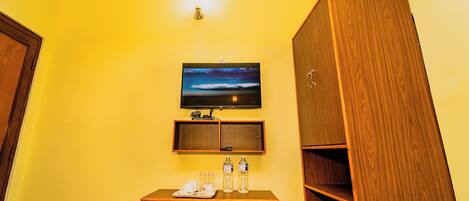 A hotel room with a wooden desk, a television mounted on the wall, and a wardrobe.
