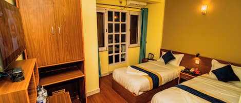 A hotel room with two beds, a wooden wardrobe, a desk with a chair, and a window with curtains.