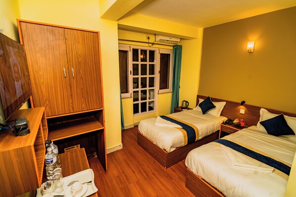 A hotel room with two beds, a wooden wardrobe, a desk with a chair, and a window with curtains.
