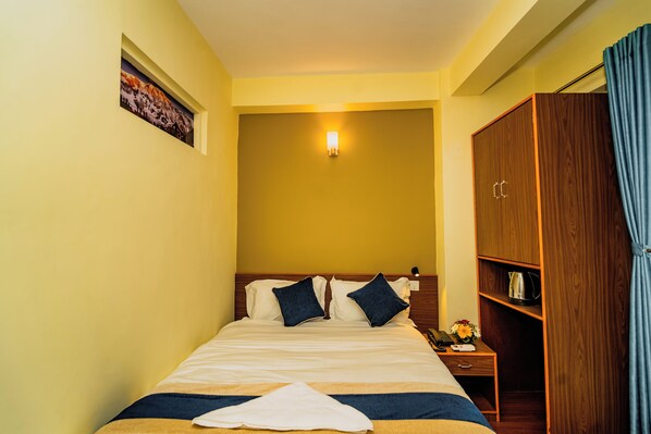 A hotel room with a bed, a nightstand, a wooden wardrobe, and a wall-mounted light fixture. - Hotel Aashraya Home Pvt. Ltd. (Kathmandu)