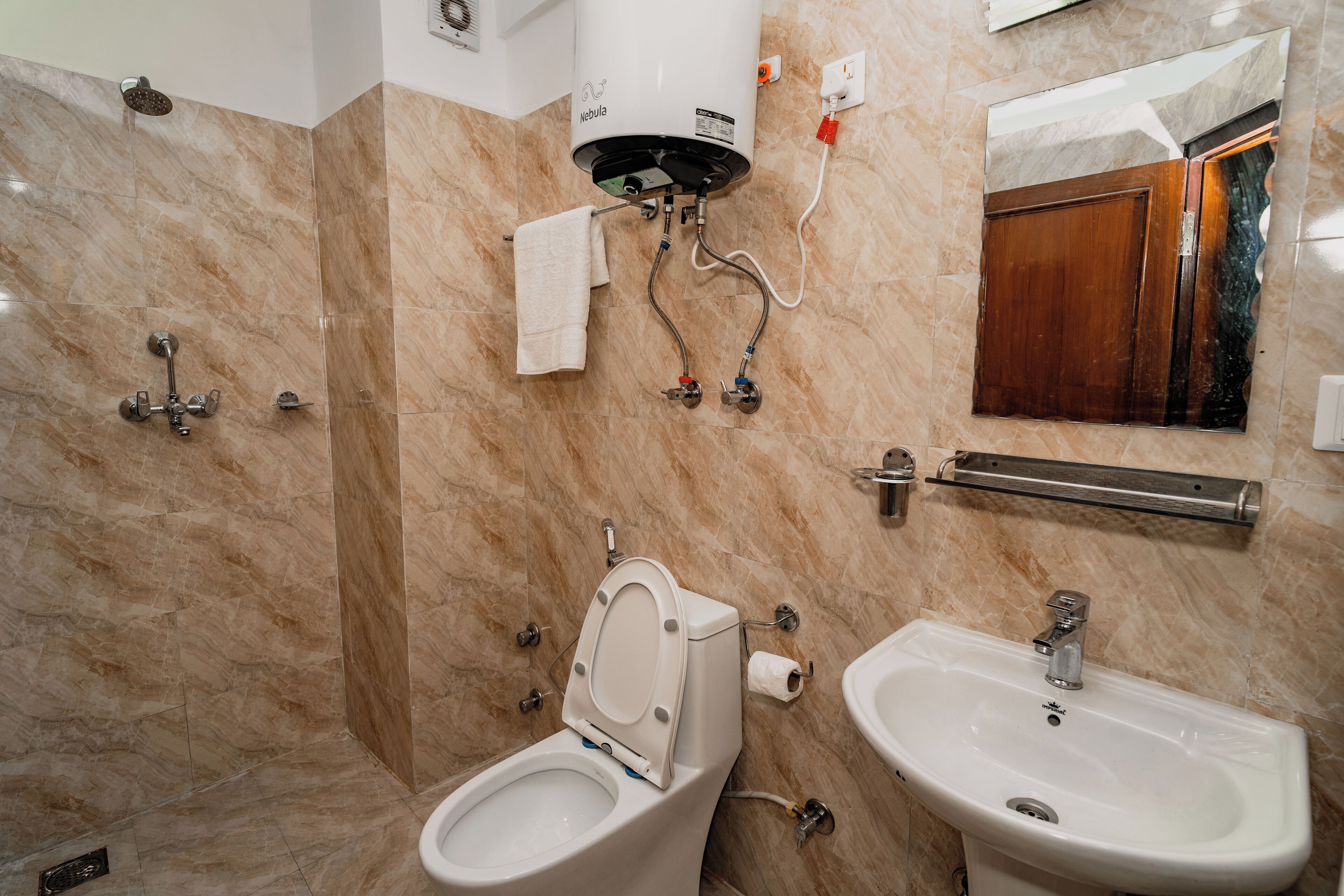 Un baño con inodoro, bidé y lavabo, todo con tuberías a la vista y un perchero para toallas.