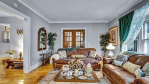 A living room with two leather sofas, a coffee table, and a large mirror. There is a window with green curtains and a door with glass panels. - Live in sophistication and elegance in your VRBO home (Rochester)