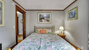 Une chambre à coucher avec une couvre-lit à motifs floraux, une table de chevet avec une lampe et des tableaux encadrés accrochés aux murs.