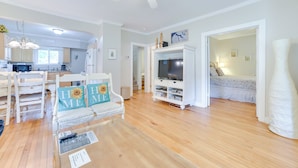 A spacious living room with a wooden floor, a white sofa with sunflower pillows, a TV stand, and a ceiling fan. - Walk to Lake Michigan: Pet-Friendly Charlevoix Gem (Charlevoix)