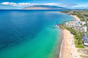An aerial view of a coastal area with a beach, clear blue waters, and a mountain in the background. - Kamaole Nalu 301 - Stunning Ocean Views, Renovated, Ocean Front, New Listing! (Kihei)