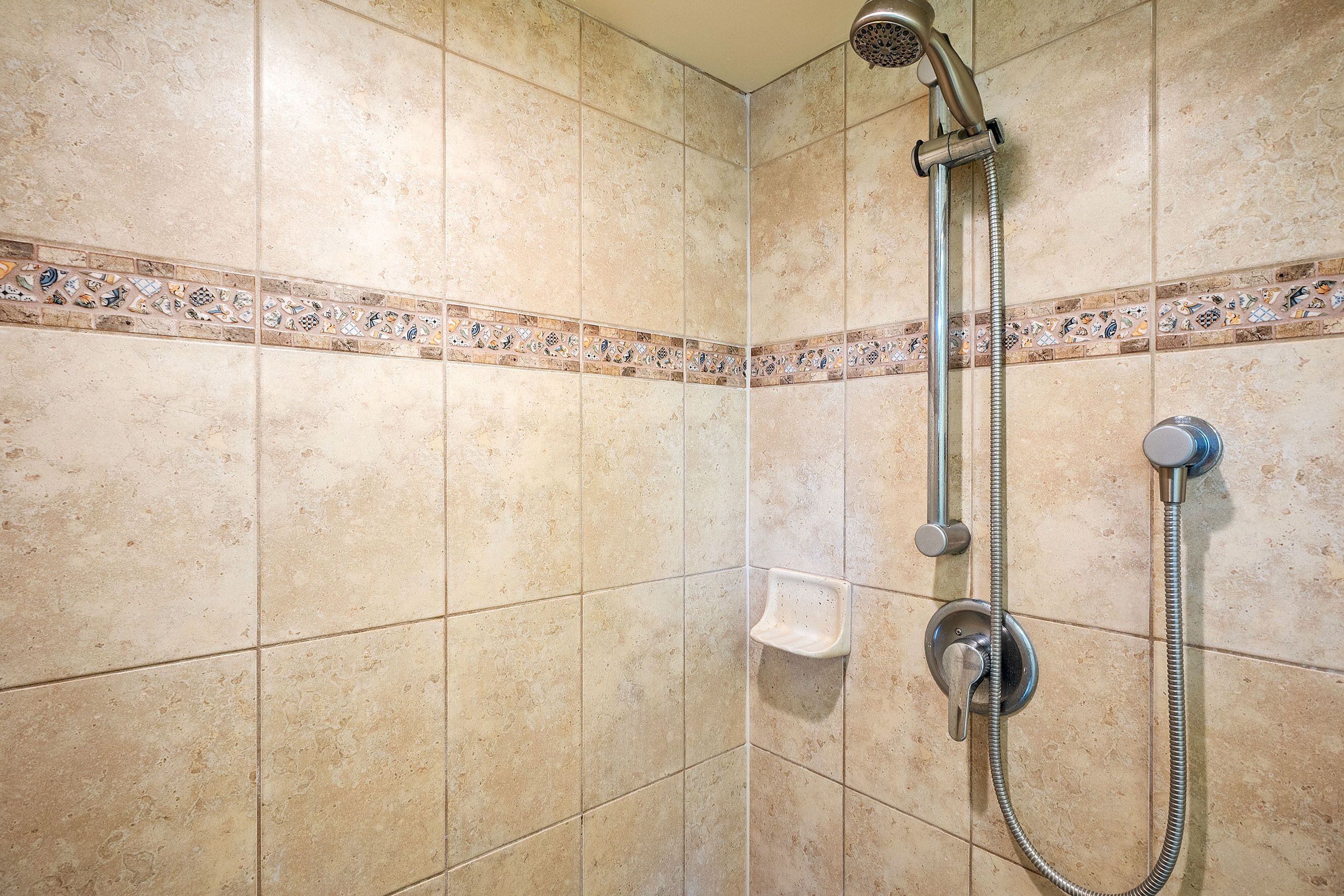 Un espace douche avec des carreaux de couleur beige, une pomme de douche et un pommeau de douche amovible.