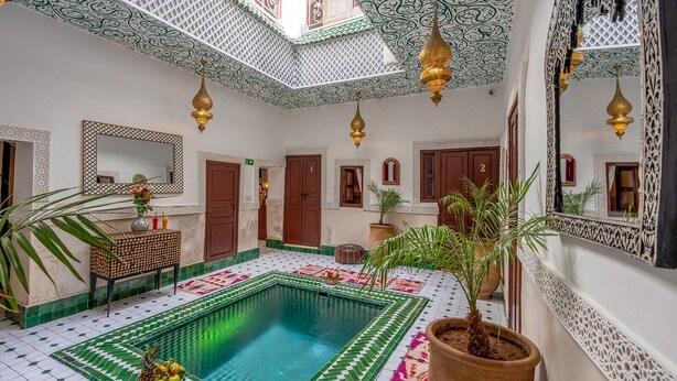 Un intérieur marocain traditionnel avec une piscine centrale, un plafond décoré et un sol carrelé.