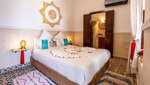 Une chambre d’hôtel avec un lit, un élément de décoration murale, une table de chevet avec une lampe, une serviette rouge et un tapis à motifs.