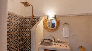 Une salle de bain avec un mur orné d’un motif géométrique, un miroir rond doté d’un cadre doré, un lavabo moderne et une douche au design original.
