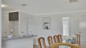A dining area with a wooden table, chairs, and a central island with a white countertop. There are two vases with flowers on the table, and a framed picture on the wall.