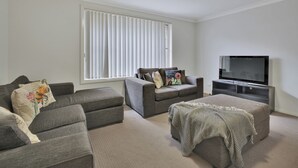 A living room with a grey sofa set, a television, and a large window with blinds.