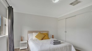 A bedroom with a bed, a nightstand, a wardrobe, and a window with curtains.