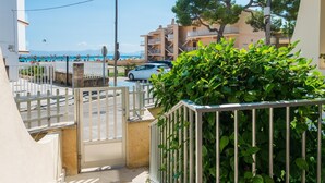 A residential street with a gated entrance, a parked car, and a view of a beach with people and umbrellas.