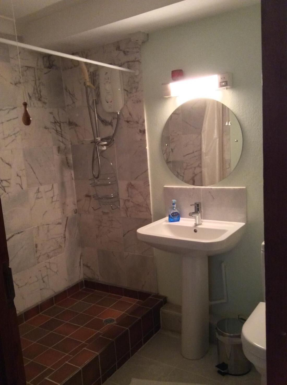 A bathroom with a marble shower, a sink with a mirror, and a toilet.