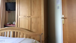 A bedroom with a wooden wardrobe, a bed with a headboard, a television mounted on the wall, and a small table with a lamp. - Room-orchard Manor, Fore Street, Nr Trur (Truro)
