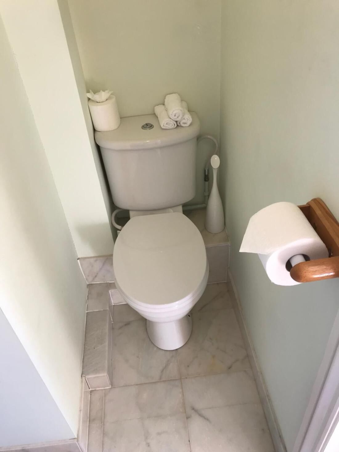 Een kleine badkamer met een toilet, toiletrolhouder en een marmeren vloer.