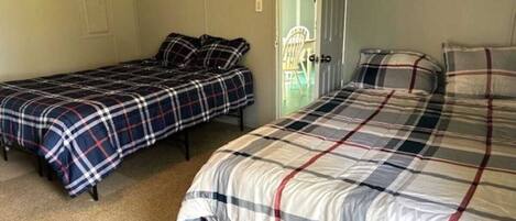 A room with two single beds and a larger bed, all with plaid bedding.