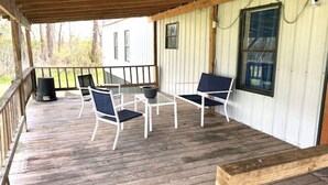 Área externa coberta com deck de madeira, corrimão de metal branco e uma mesa com cadeiras.