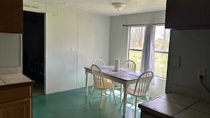 A dining area with a table and chairs, a window with curtains, and a door leading to another room.