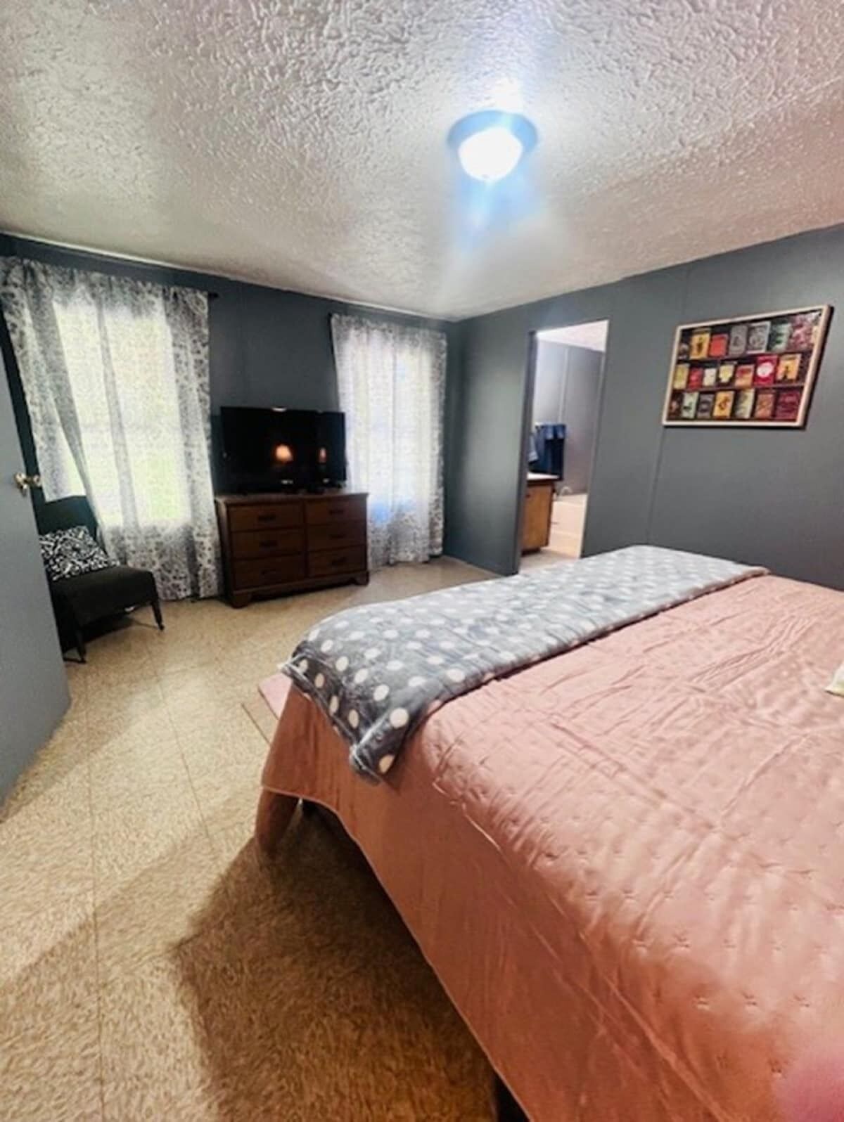 A bedroom with a bed, a dresser, a television, and a wall with framed pictures.